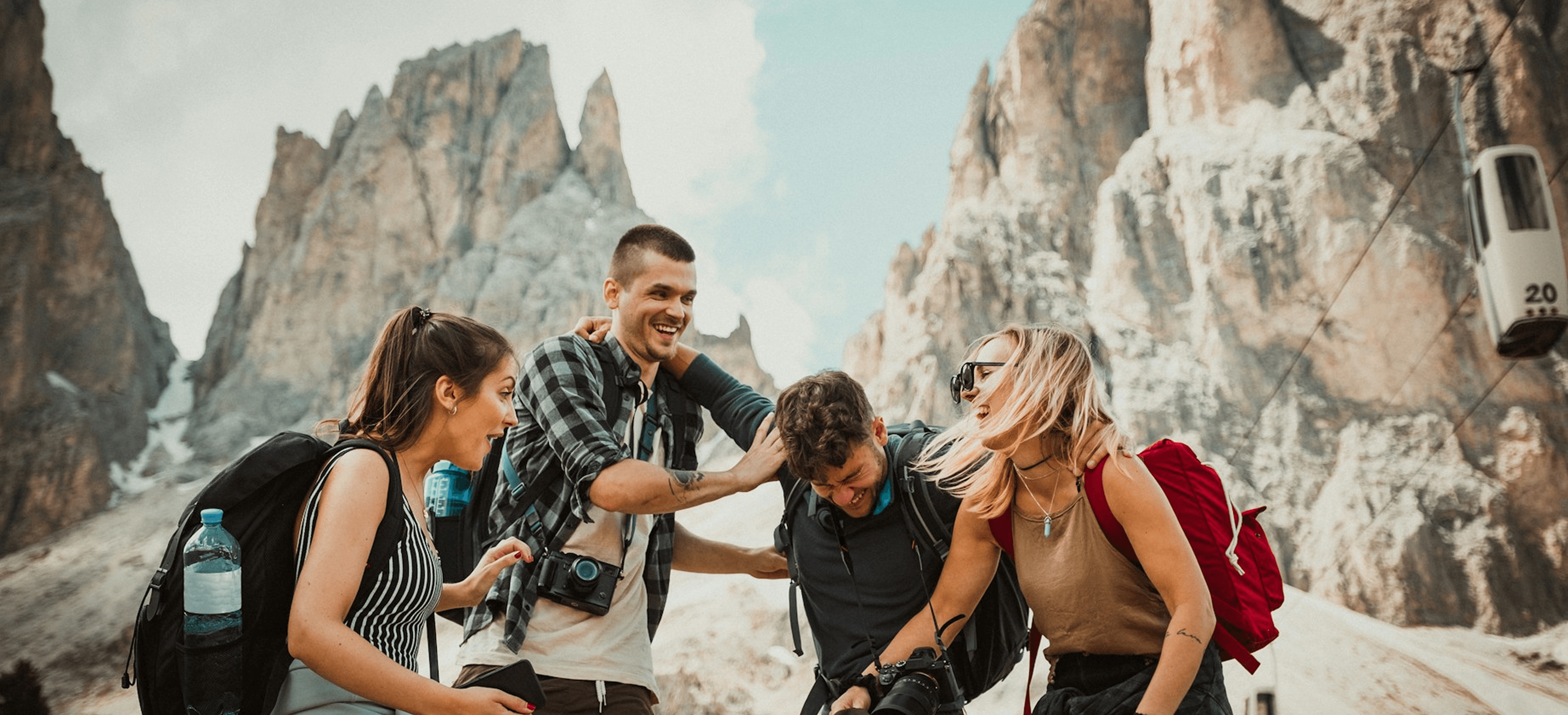 Travelers with arms raised overlooking a valley with hot air balloons at dawn